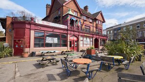 A red building with a balcony, outdoor seating, and a signboard. - Hootananny Hostel (London)