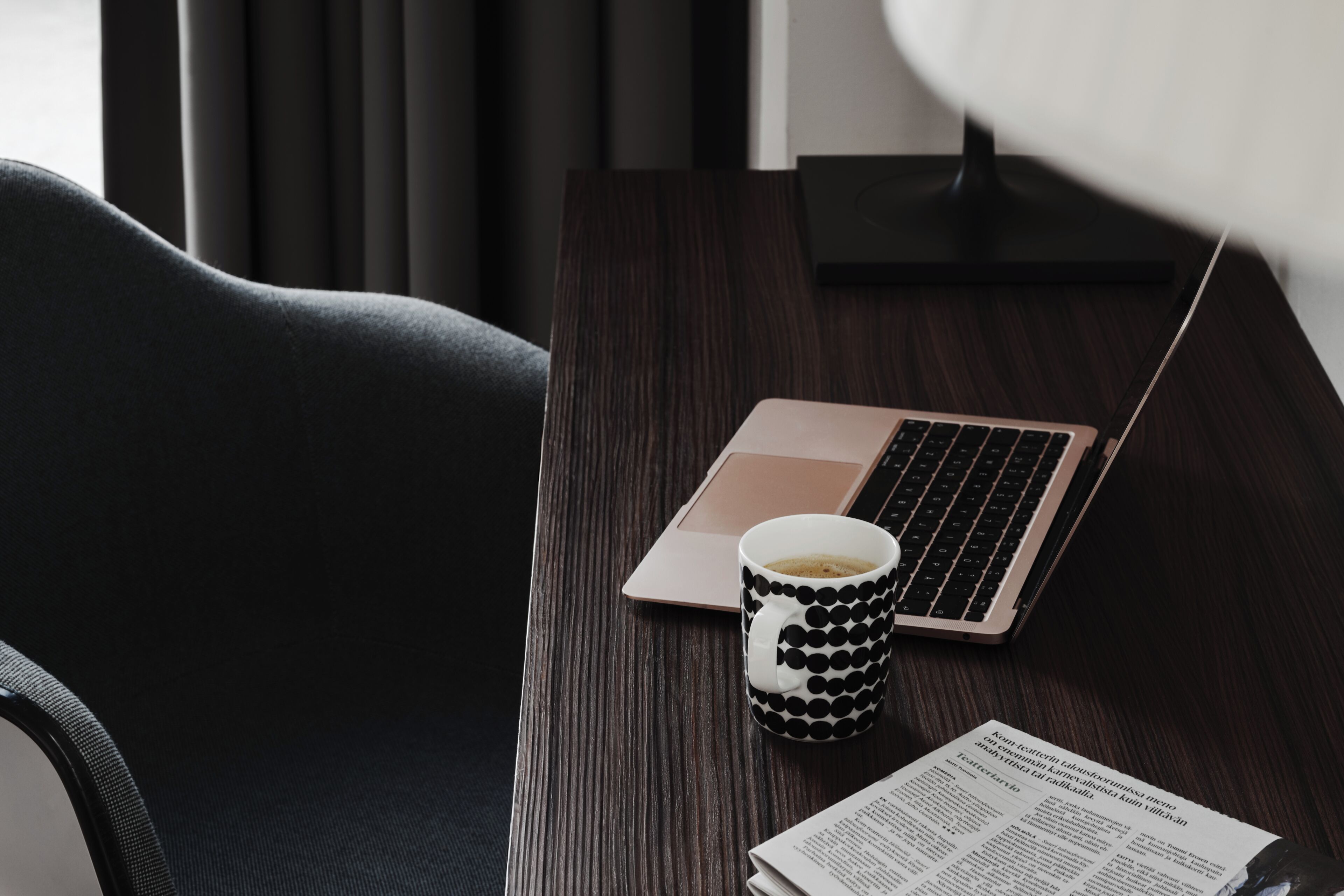 A laptop, a polka-dotted mug, and a document on a wooden table.