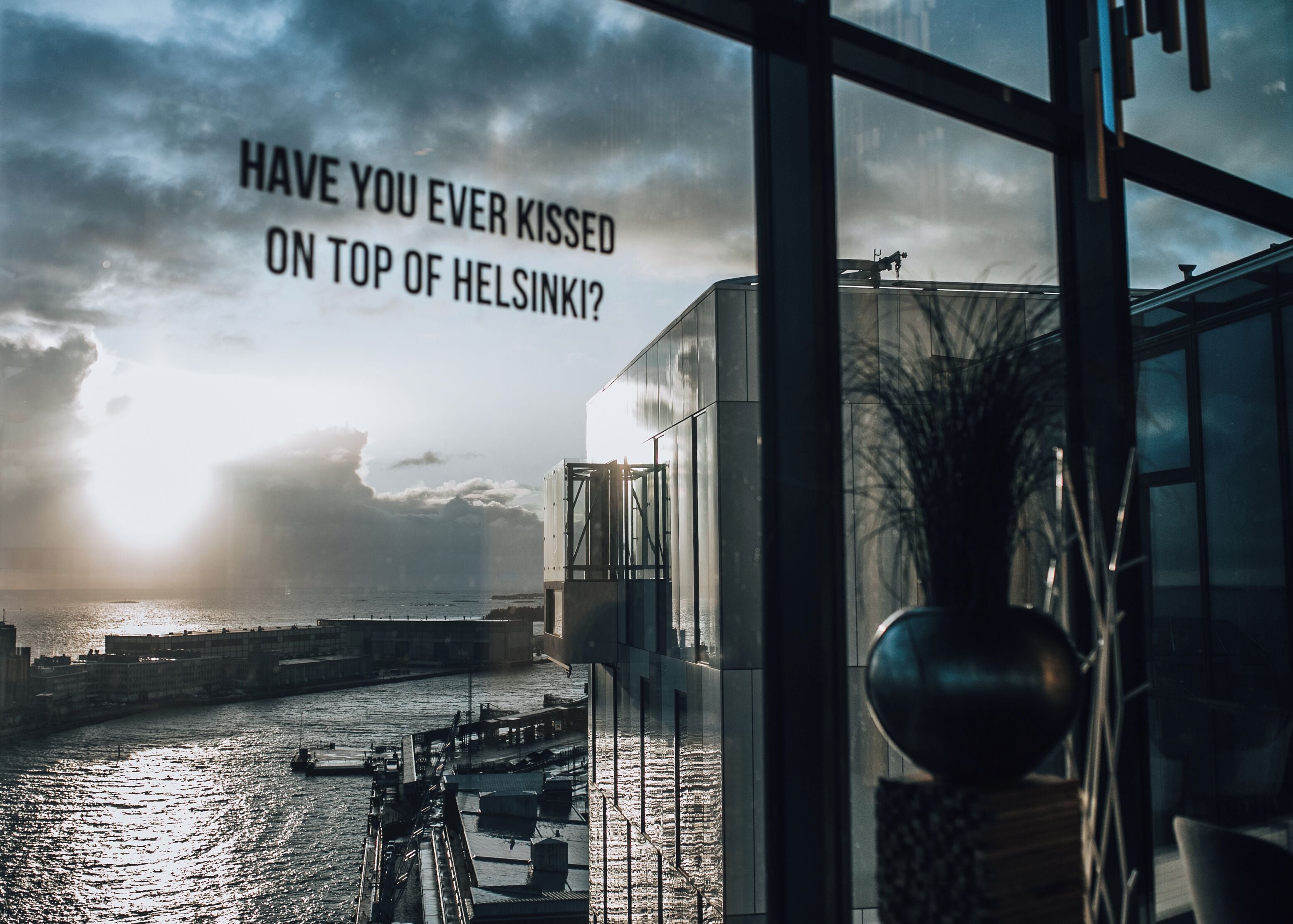 En vy från insidan av en byggnad med utsikt över en hamn, och en fråga om att kyssa någon på toppen av ett högt hus i Helsingfors.