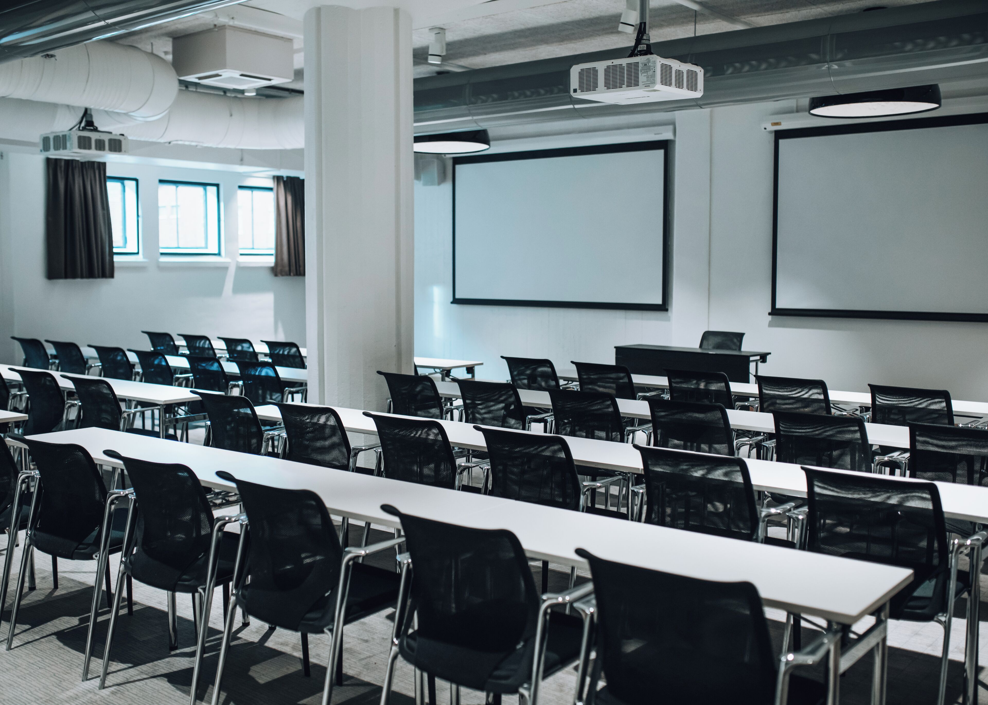 A conference room with rows of tables and chairs, a projector, and a screen.