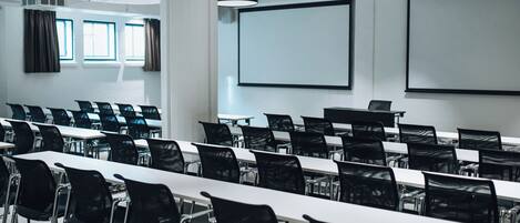 A conference room with rows of tables and chairs, a projector, and a screen.