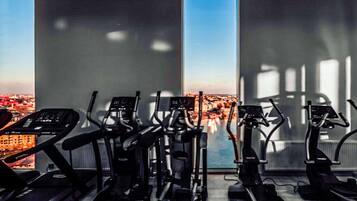 Ett gym med flera löpband och annan träningsutrustning, stora fönster med utsikt över staden.