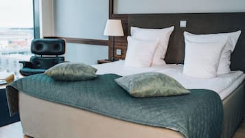 Una habitación de hotel con una cama grande, dos almohadas, una silla, una mesita de noche y una lámpara.