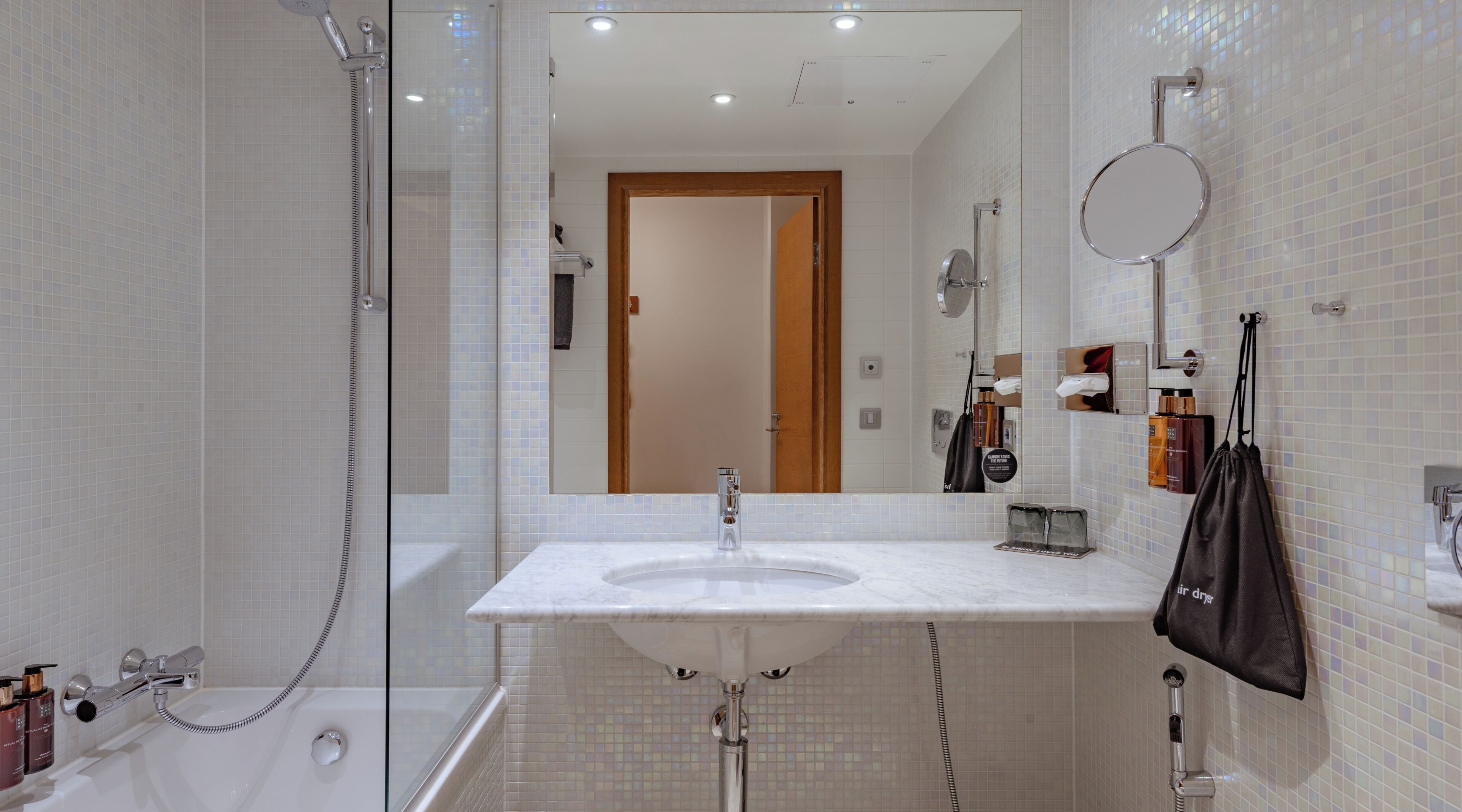 A modern bathroom with a glass-enclosed shower, a white sink, a mirror, and toiletries.