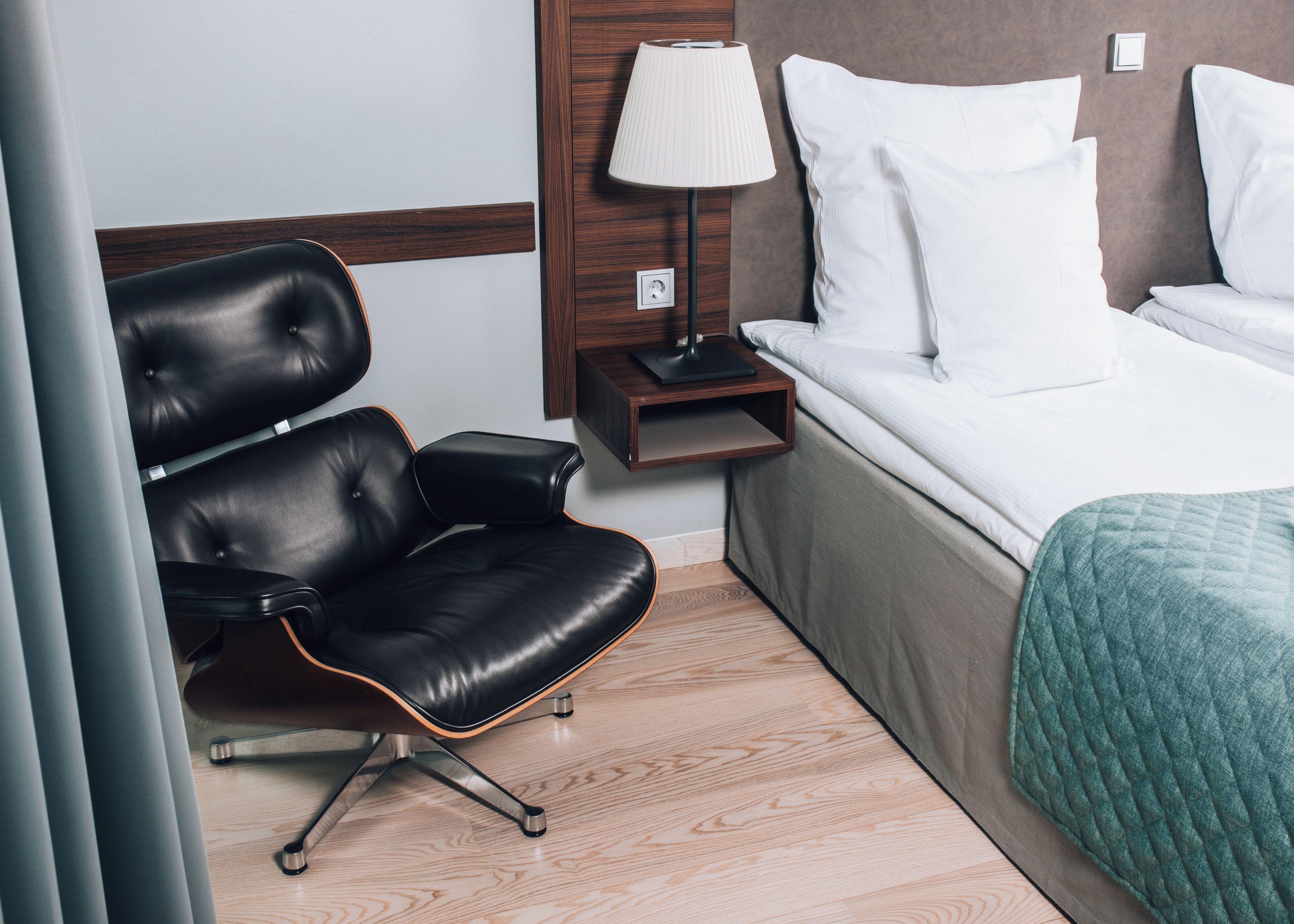 A hotel room with a bed, a chair, a nightstand, and a lamp.