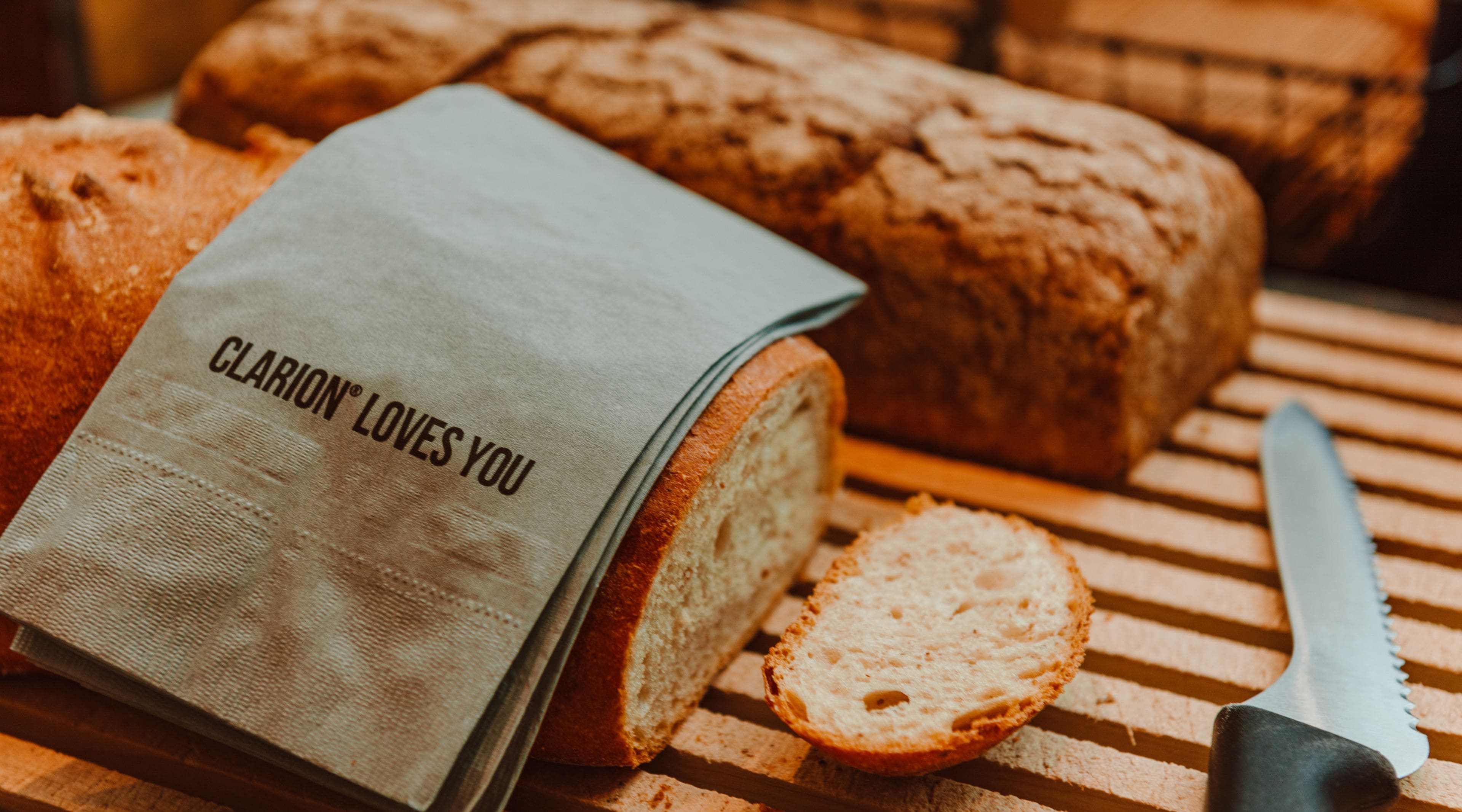 A loaf of bread with a cloth that reads "CLARION LOVES YOU" and a knife on a wooden surface.