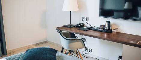 A hotel room with a bed, a desk with a lamp, a chair, a TV, and a coffee maker.