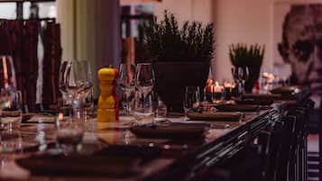 Un ambiente de restaurante con una mesa larga, copas de vino, platos y una planta en maceta.