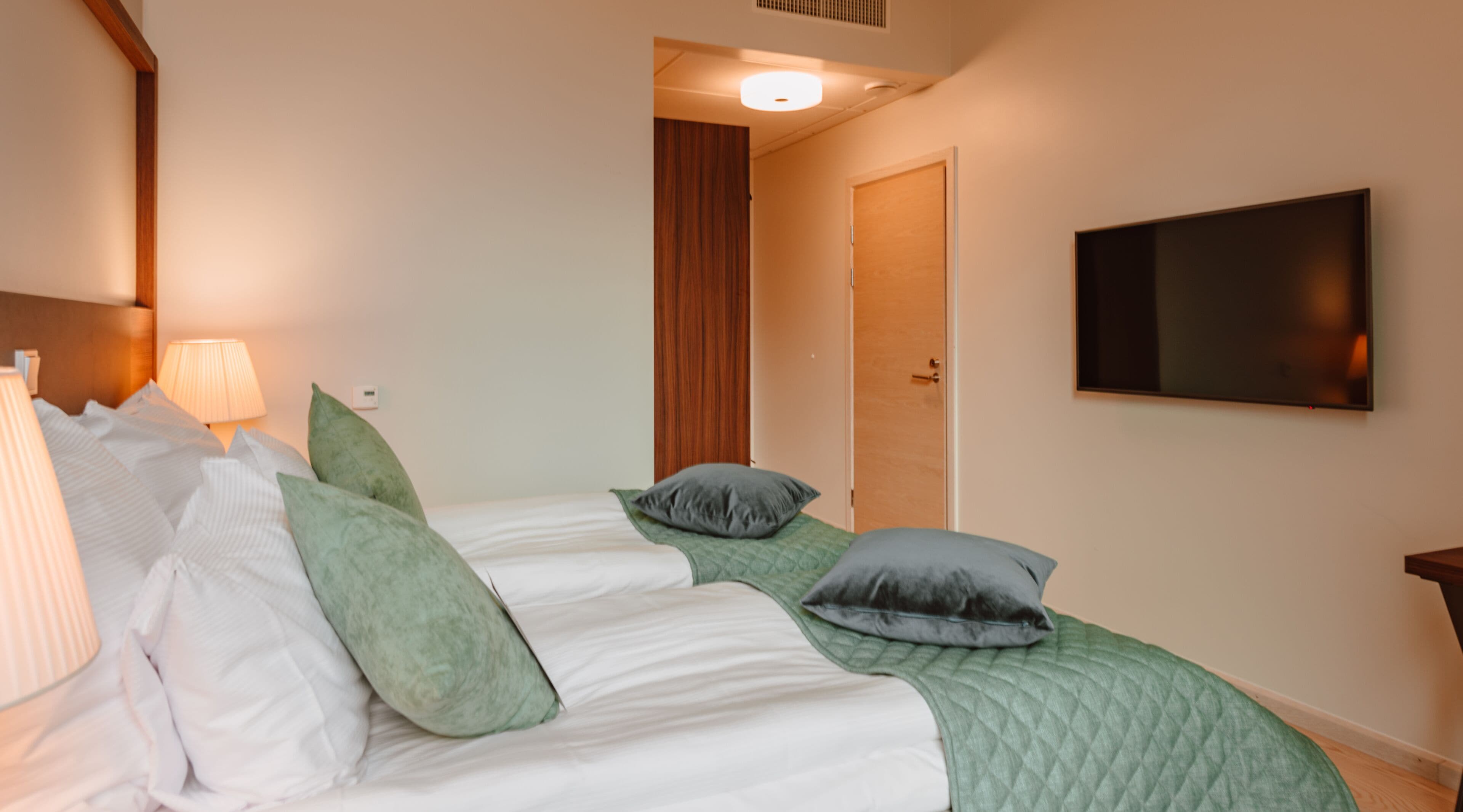 A hotel room with two beds, a TV mounted on the wall, and a door leading to another room.