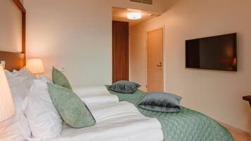 Une chambre d’hôtel avec deux lits, un téléviseur fixé au mur et une porte donnant sur une autre pièce.