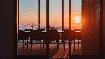 A view from inside a building with a table and chairs facing a sunset over a body of water.