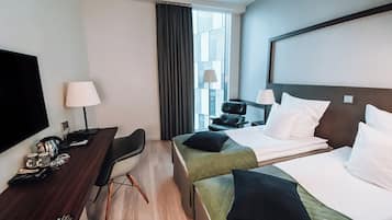 A hotel room with two beds, a desk, a chair, a TV, and a window with curtains.
