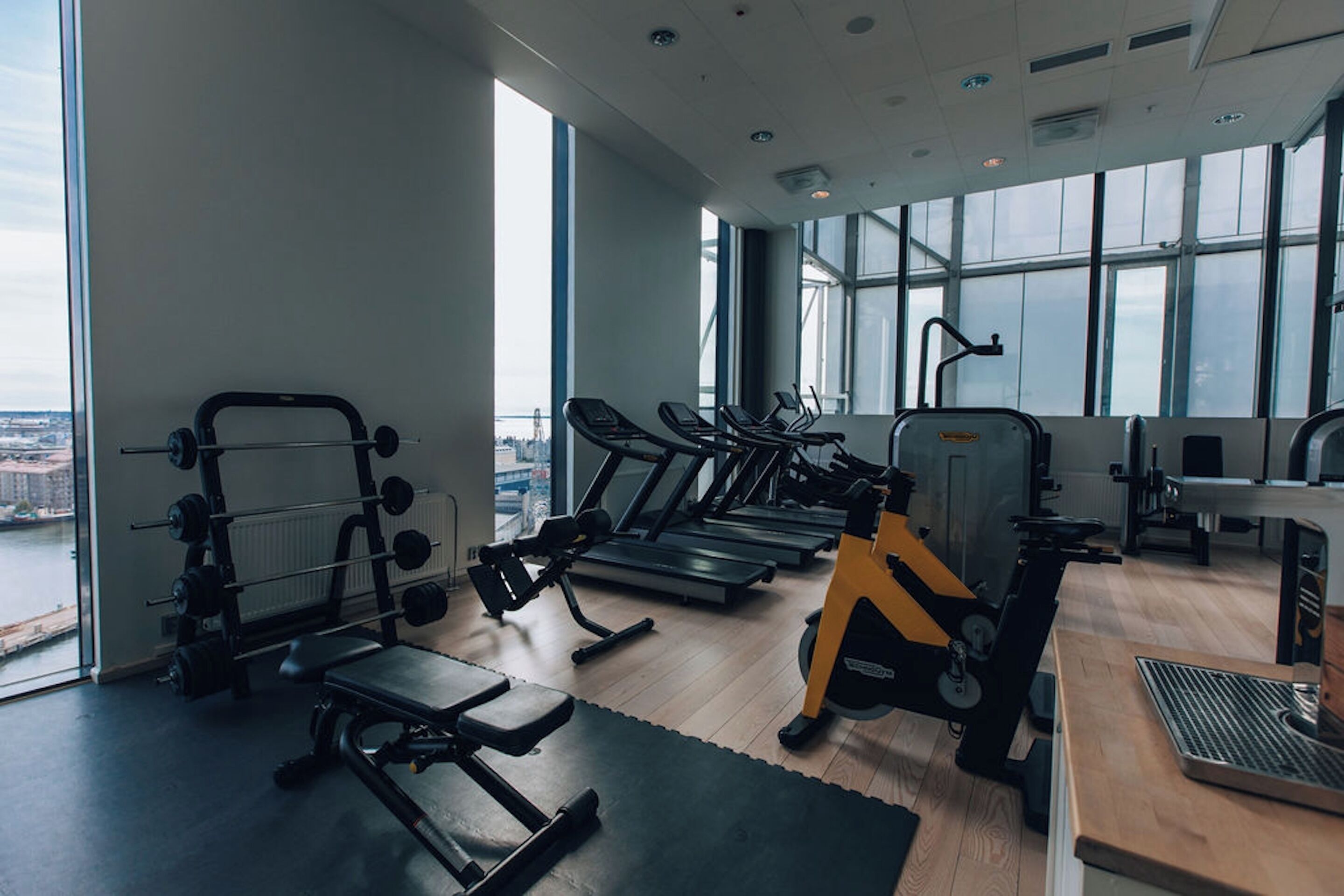 A gym with cardio machines, weightlifting equipment, and a view of the city through large windows.
