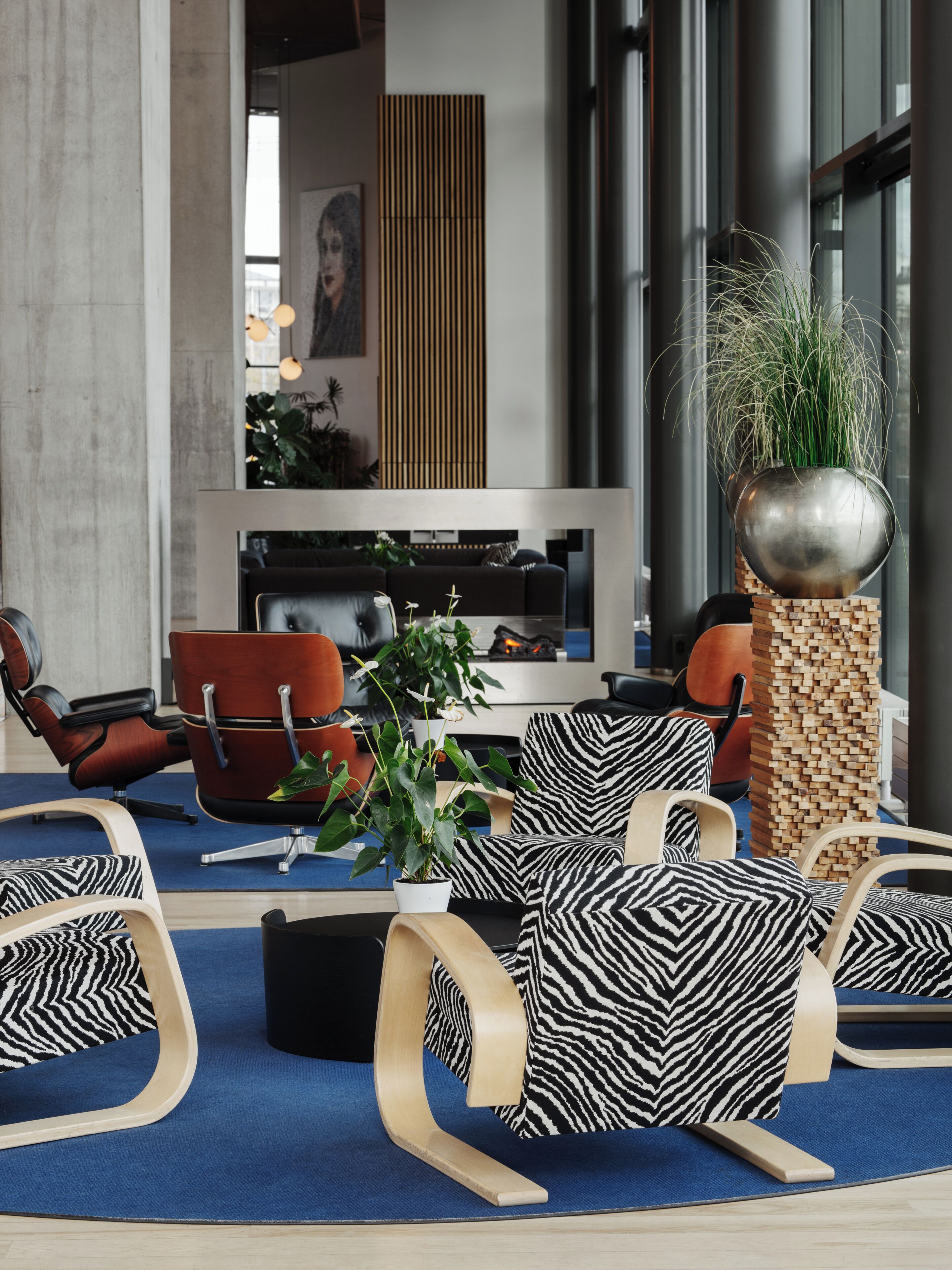 A modern lounge area with leather chairs, a blue carpet, and a large potted plant.