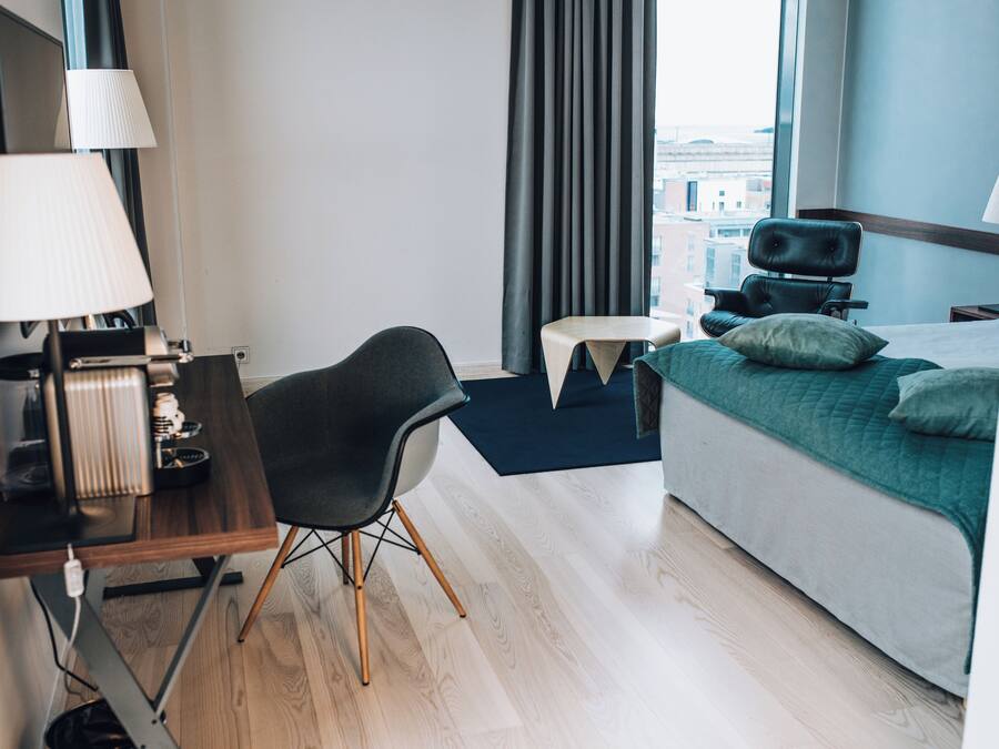 Moderni hotellihuone, jossa on sänky, työpöytä, tuoli ja näkymä kaupunkiin.