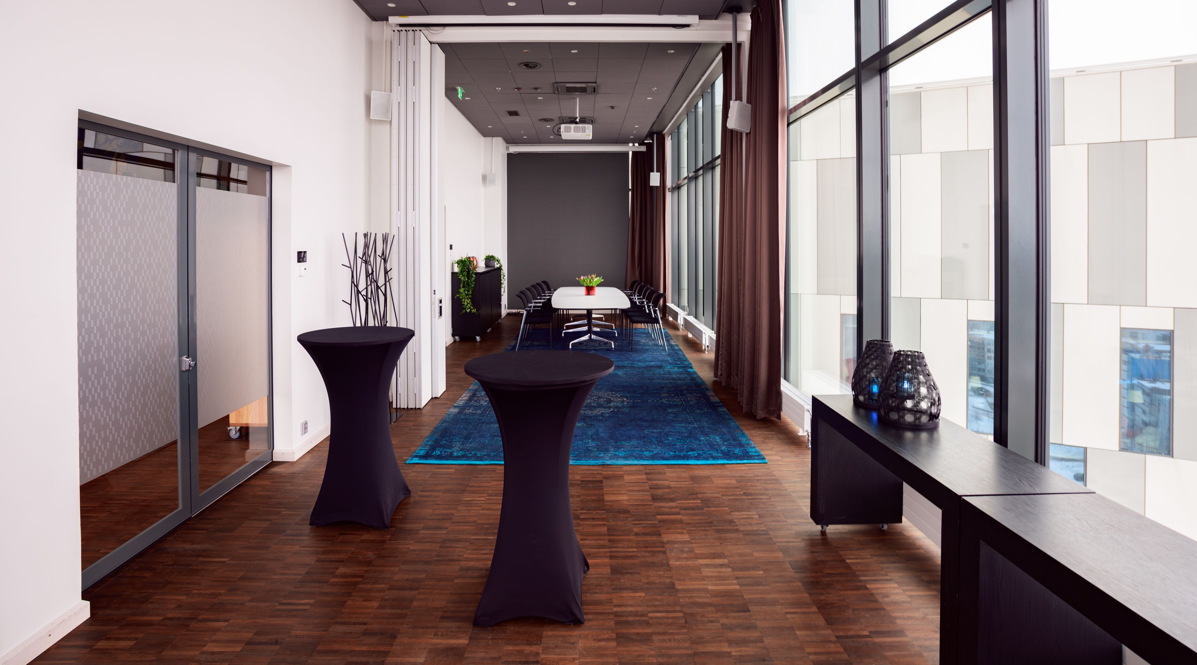 Una sala de conferencias moderna con una mesa larga, dos mesas redondas y una alfombra azul.