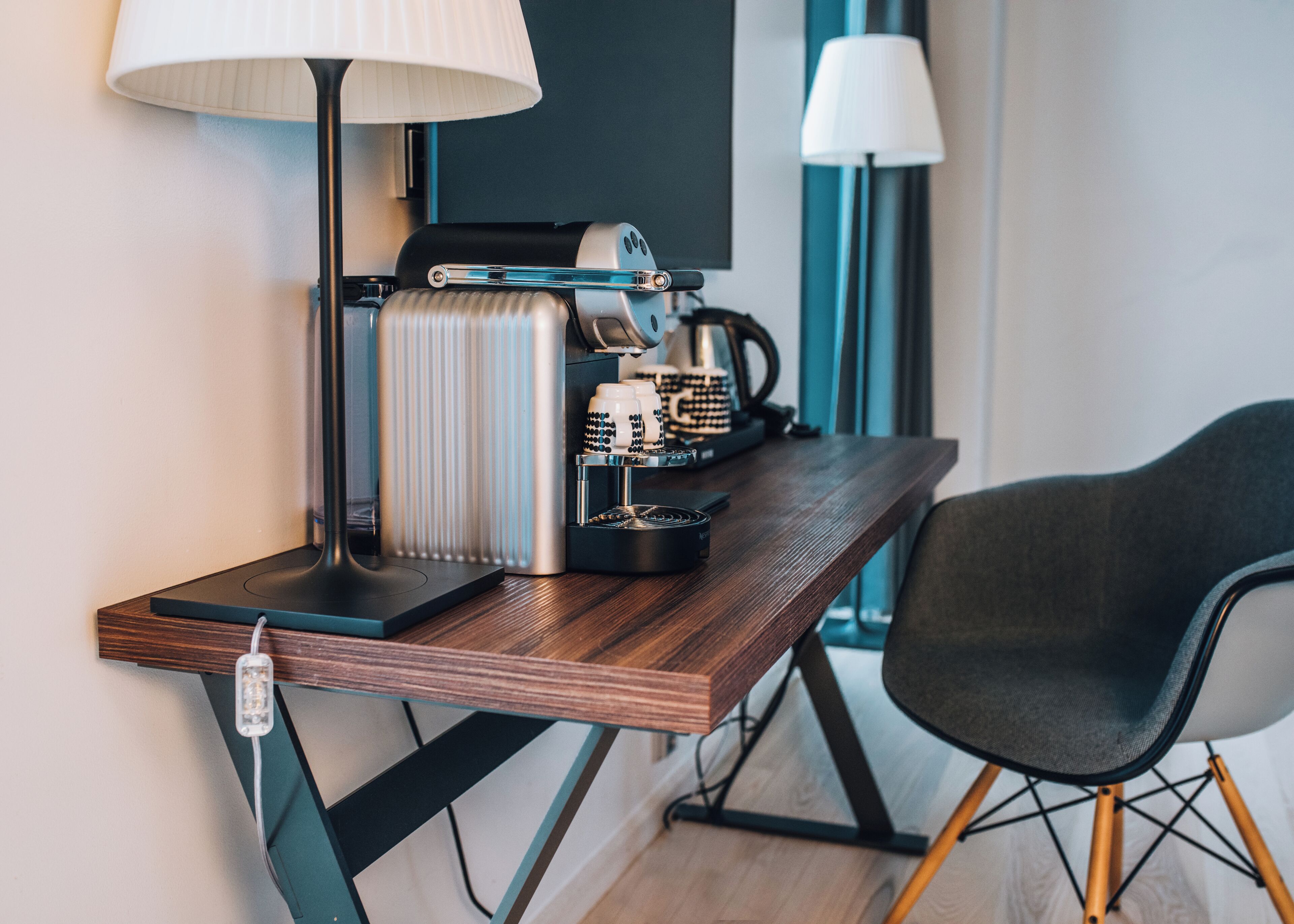 Una habitación moderna con un escritorio de madera, una cafetera, una lámpara y una silla.