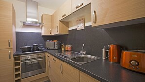 A compact kitchen with wooden cabinets, a built-in oven, a stainless steel sink, and a toaster. - Printworks Apart-Hotel (Peterhead)