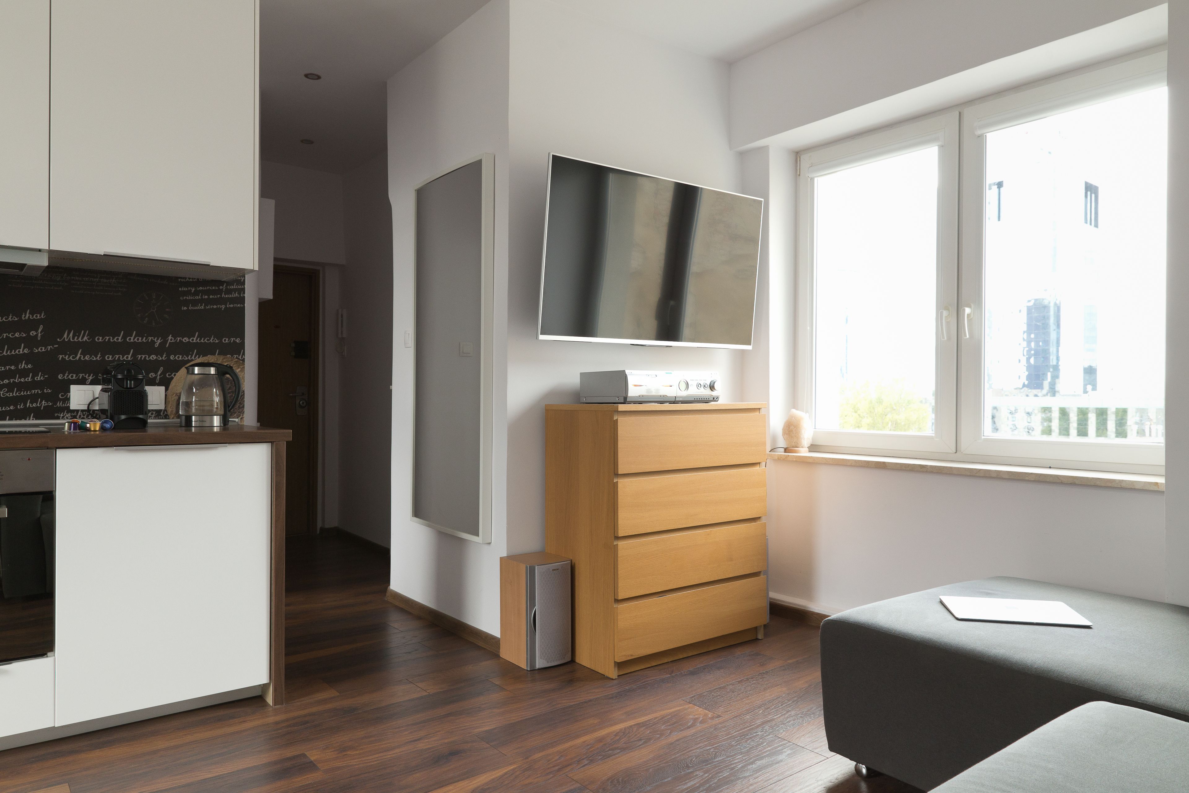 A modern kitchen with wooden cabinets, a built-in coffee machine, and a flat-screen TV mounted above a wooden dresser.