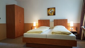 Una habitación de hotel con una cama grande, cabecera de madera, dos mesitas de noche con lámparas, un armario y un cuadro en la pared.