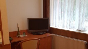Una oficina pequeña y privada con un escritorio, una silla y una computadora. Hay una ventana con cortinas translúcidas y un radiador debajo.