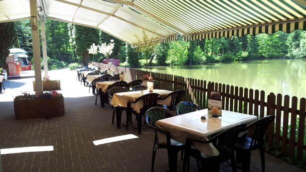 Un espacio exterior para comer con mesas y sillas, una valla de madera y vistas a un lago.