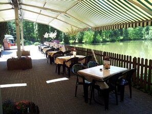 Un espace extérieur aménagé pour les repas, avec des tables et des chaises, une clôture en bois et une vue sur un lac.