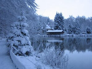 Een rustig winterlandschap met een met sneeuw bedekte meer, bomen en een rustiek gebouw aan het water.