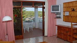 Un salon équipé d’un téléviseur, d’un meuble en bois et offrant une vue sur un balcon avec des chaises.