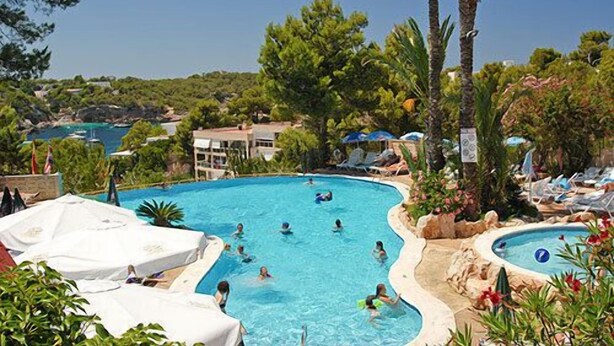 Une piscine où se baignent des personnes, entourée d’arbres et bordée d’un bâtiment.