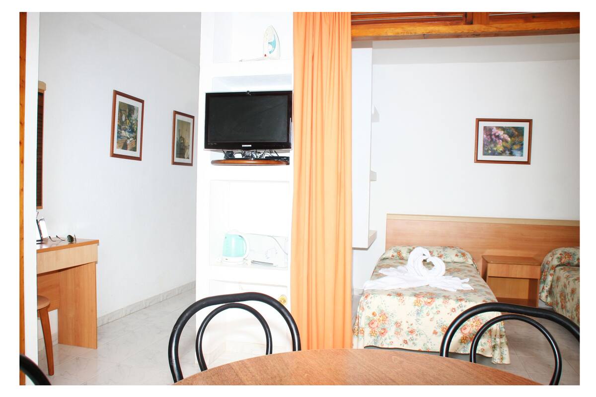 A hotel room with a wooden desk, a television, a bed with floral bedding, and two framed pictures on the wall.