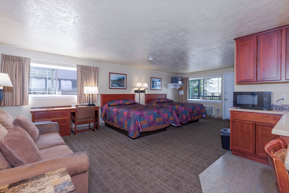 A hotel room with a bed, a desk, a couch, a TV, and a kitchen area.