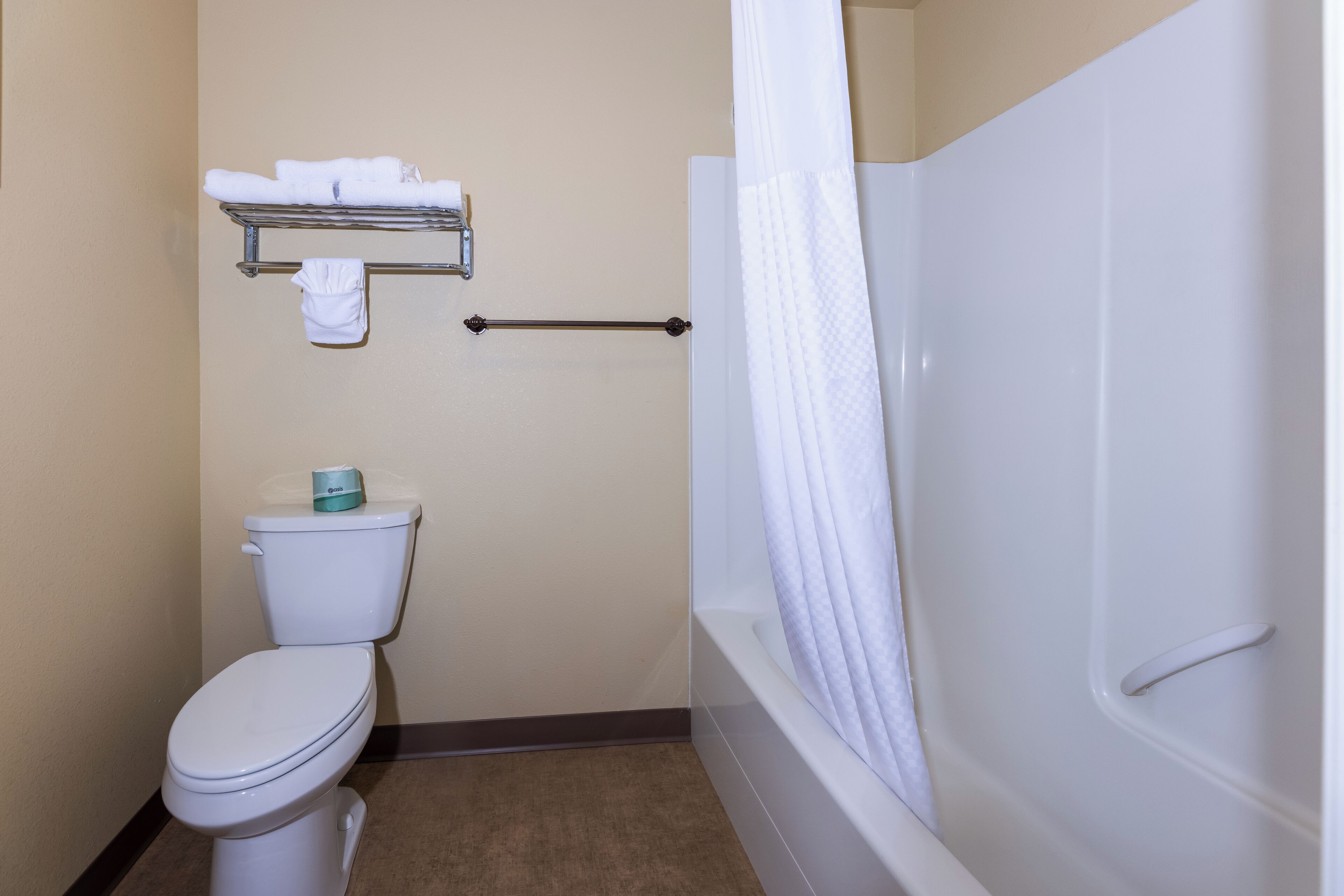 Een badkamer met toilet, een handdoekrek met handdoeken en een bad met douchegordijn.