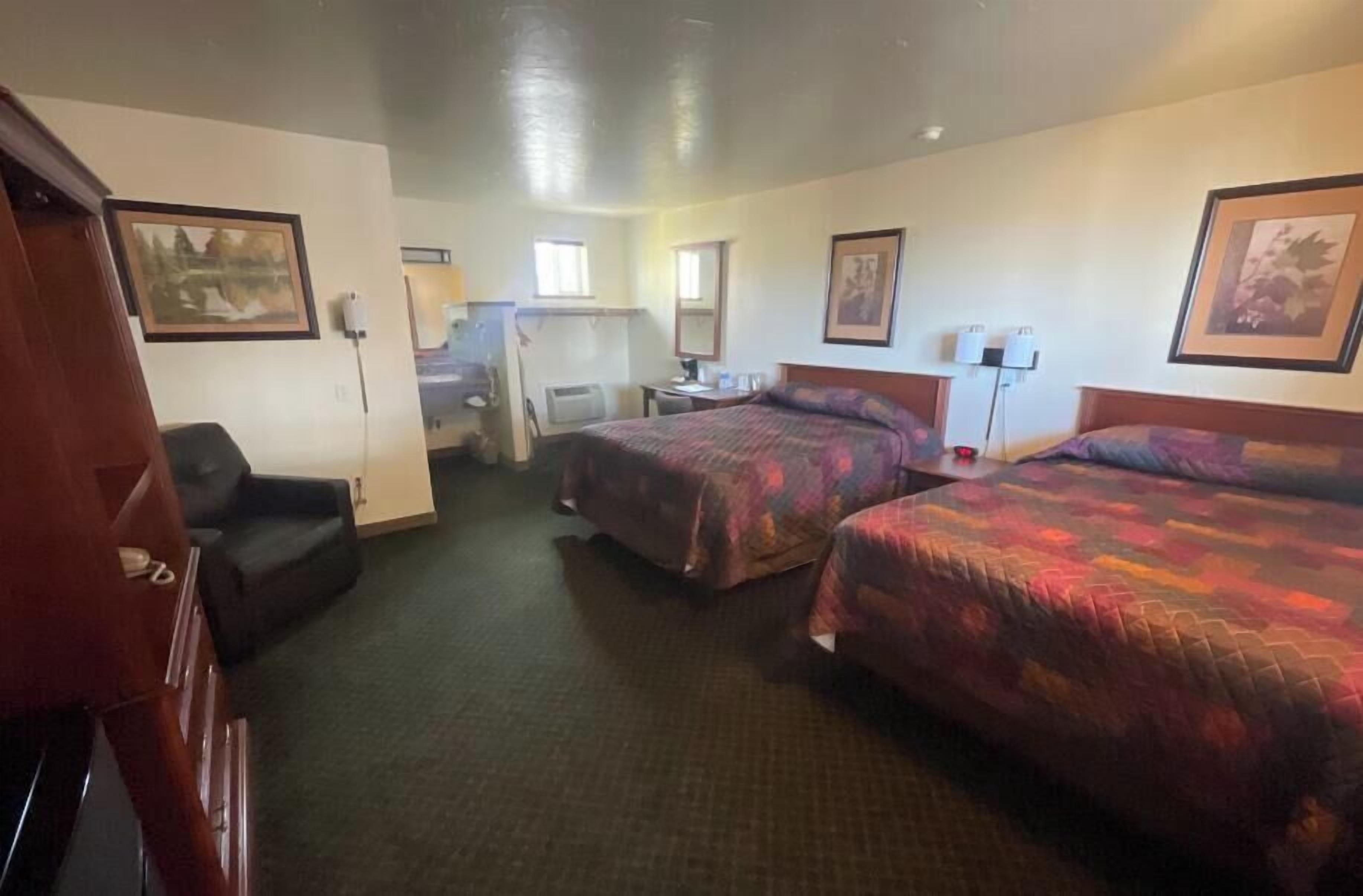 A hotel room with two beds, a desk, a chair, and a small kitchenette.