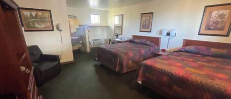 Une chambre d’hôtel avec deux lits, un bureau, une chaise et une petite kitchenette.