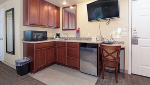 A compact kitchen with wooden cabinets, a built-in microwave, a dishwasher, and a flat-screen TV mounted above the counter. - Gateway Inn (Grangeville)
