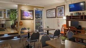 A hotel dining area with multiple tables and chairs, a television, and framed artwork on the walls. - Gateway Inn (Grangeville)