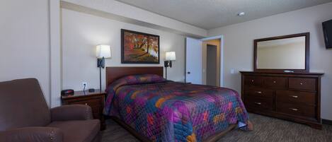 A hotel room with a large bed, a brown leather chair, a dresser, and a painting on the wall.