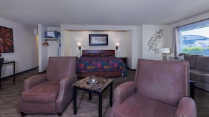 A hotel room with a bed, two armchairs, a small table, and a window with a view. - Gateway Inn (Grangeville)