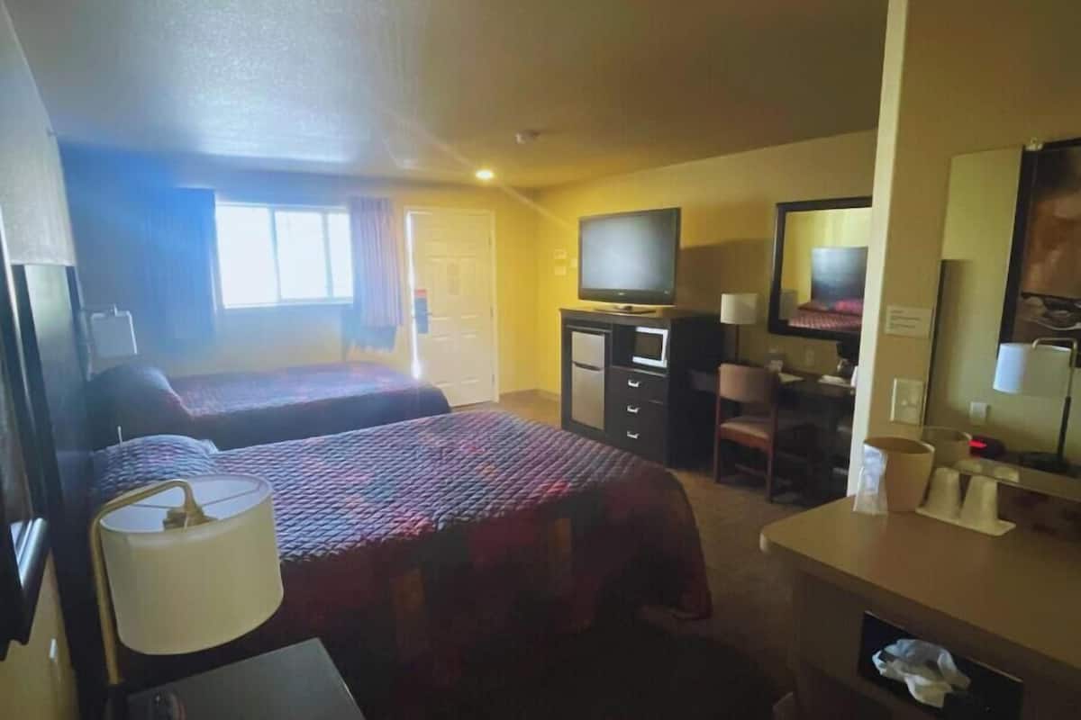 A hotel room with two beds, a TV, a desk with a chair, and a mirror.