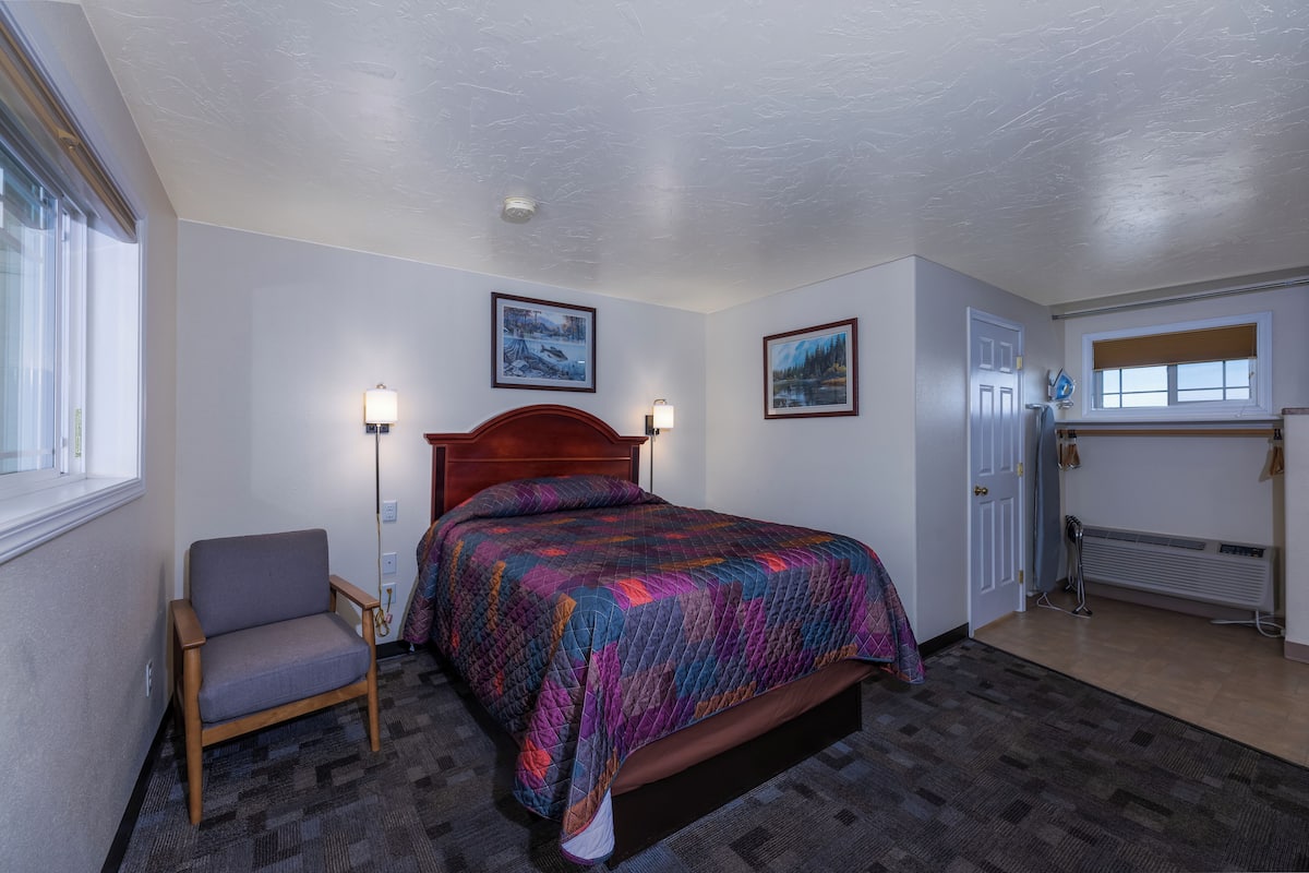A bedroom with a bed, a chair, a radiator, and two wall-mounted lamps.
