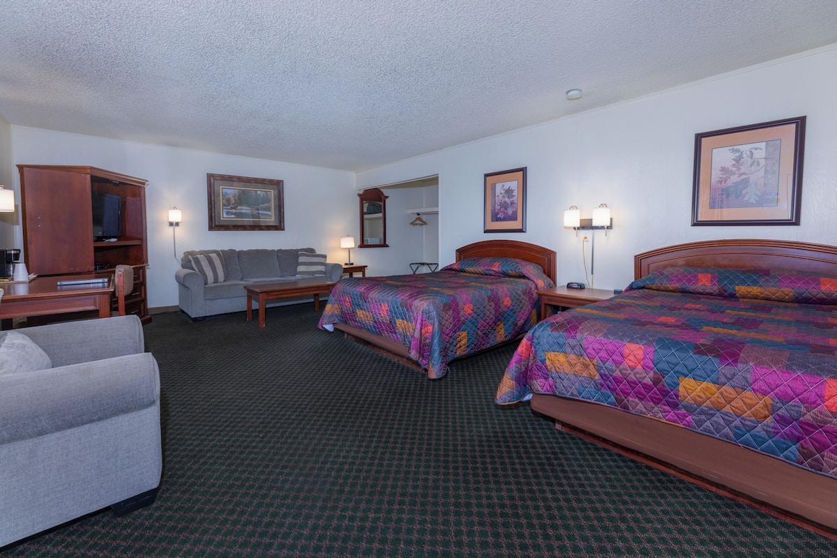 A hotel room with two beds, a sofa, a desk, and a TV.