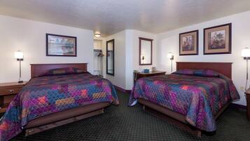 Quarto de hotel com duas camas, cada uma com um colcha colorida, uma mesinha de cabeceira, um espelho e quadros nas paredes.