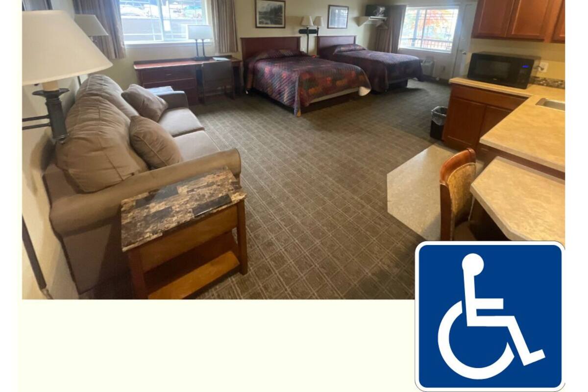 A hotel room with a sofa, two beds, a desk, and a kitchenette.