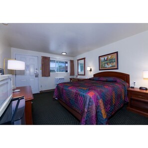 A hotel room with a bed, a desk with a lamp, a television, a window with curtains, and a painting on the wall.