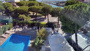 A pool area with lounge chairs and umbrellas, surrounded by trees and a view of the marina. - Hotel Franca (Cervia)
