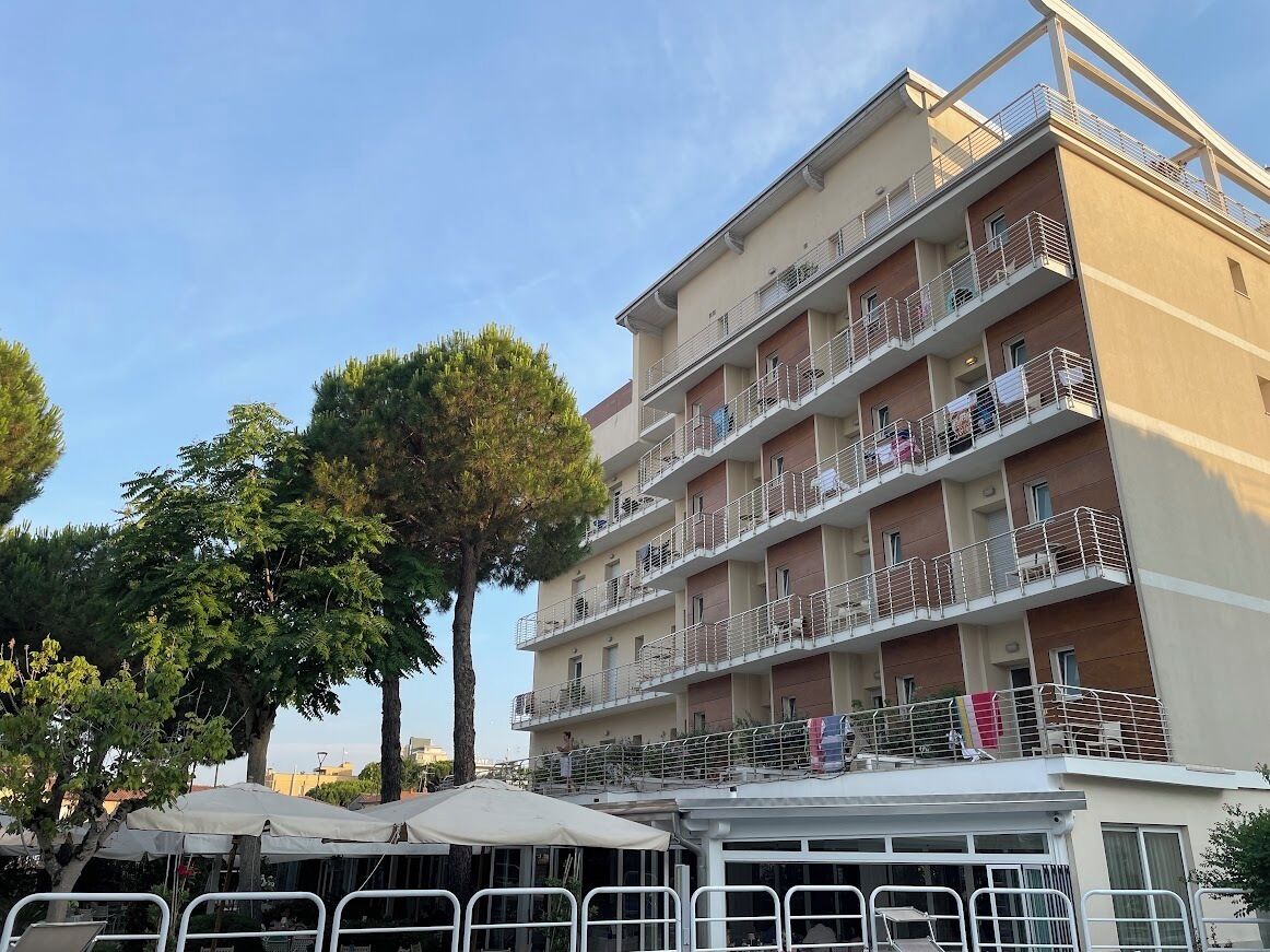 Un immeuble résidentiel à plusieurs étages, doté de balcons, avec un ciel dégagé et des arbres au premier plan.