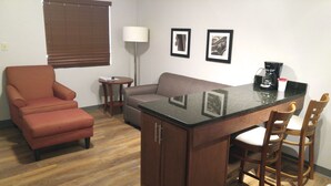 A compact living space with a kitchenette, a sofa, a single armchair, and a small table.