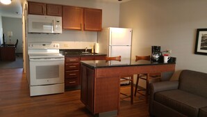 A compact kitchen with wooden cabinets, a white refrigerator, a microwave, and a stove. There is a small dining area with a table and chairs.
