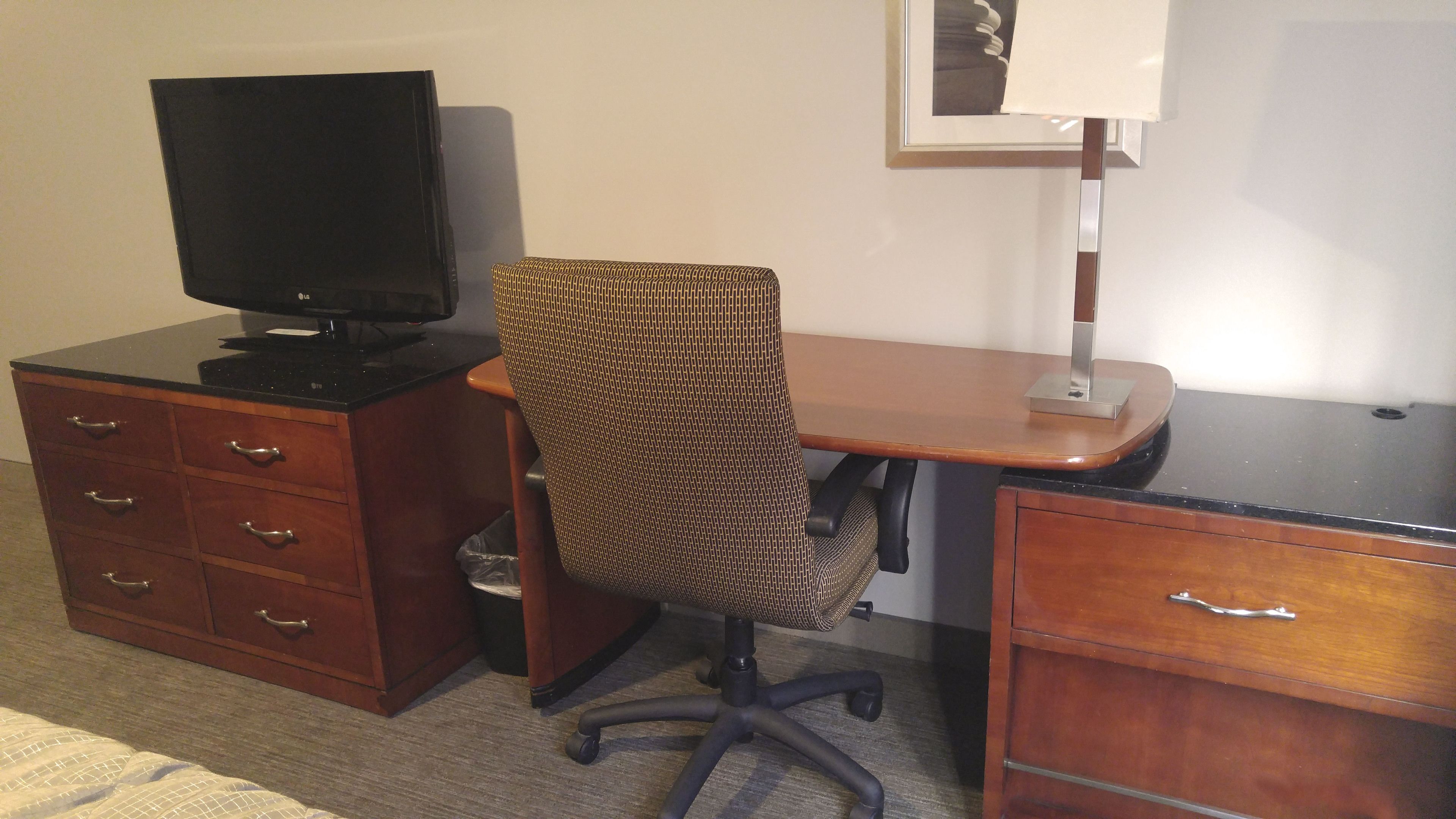Une chambre d’hôtel avec un bureau en bois, un ordinateur, une chaise et un petit meuble de rangement.